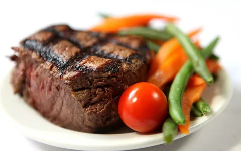Steak with vegetables on a white plate.