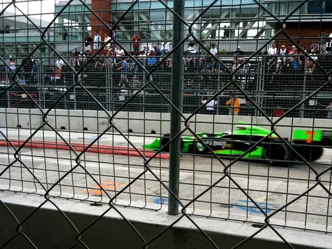 Green race car passing the fenced street circuit.