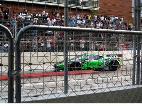 Green race car passing spectators behind the fence.