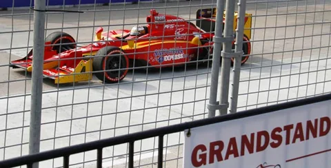 Red and yellow race car behind the grandstand fence.